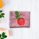 Pink towel with red apple and green leaf embroidery on light wooden background