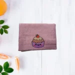 Purple towel with cute smiling cupcake embroidery topped with strawberry