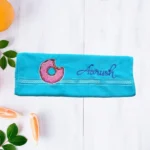 Turquoise towel with pink bitten donut embroidery on light wooden background