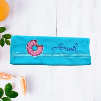 Turquoise towel with pink bitten donut embroidery on light wooden background