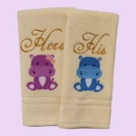 Cream towels with “Hers” and “His” embroidery and cute pink and blue hippos on pastel background