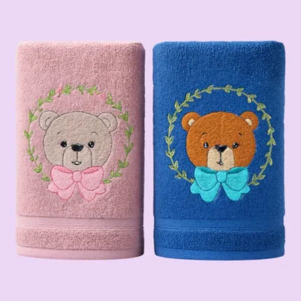 Pink and blue towels with cute bear faces and bows embroidered inside leaf wreaths on pastel background