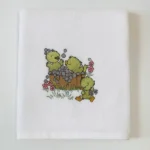 White towel with three yellow ducklings playing in a wooden tub of bubbles and flowers
