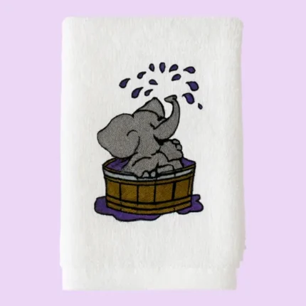 White towel with grey elephant splashing water in a wooden tub on pastel background