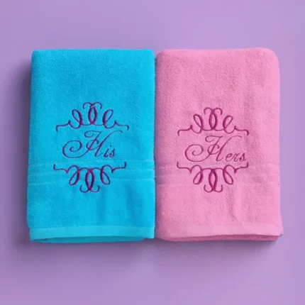 Blue and pink towels with decorative “His” and “Hers” embroidery on pastel background
