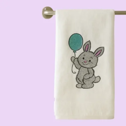 White towel hanging on rail with cute grey bunny holding a teal balloon
