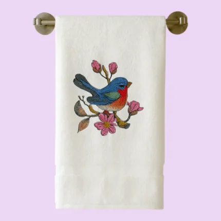 White towel hanging on rail with blue and red bird embroidery perched on pink flowers